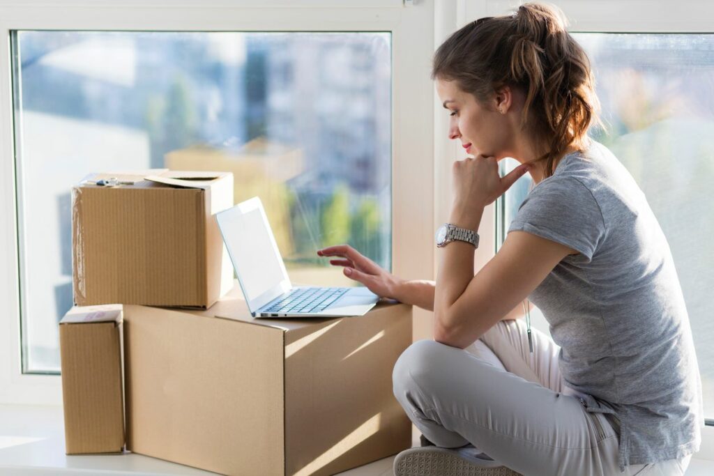 Woman with laptop on cardboard boxes researching storage options