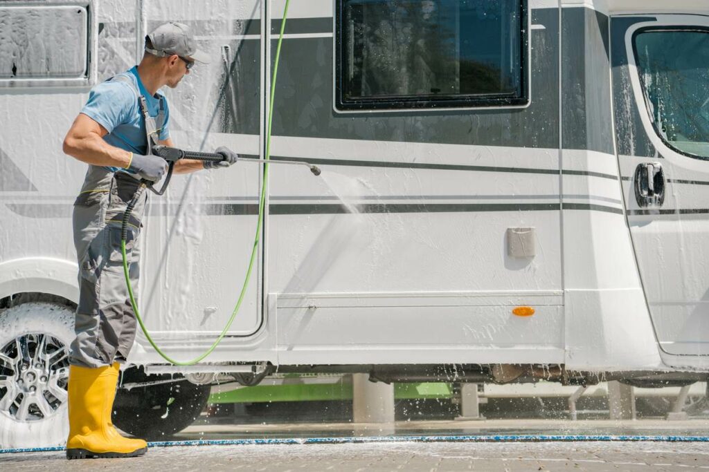A man in yellow rubber boots and a hat pressure-washes an RV.