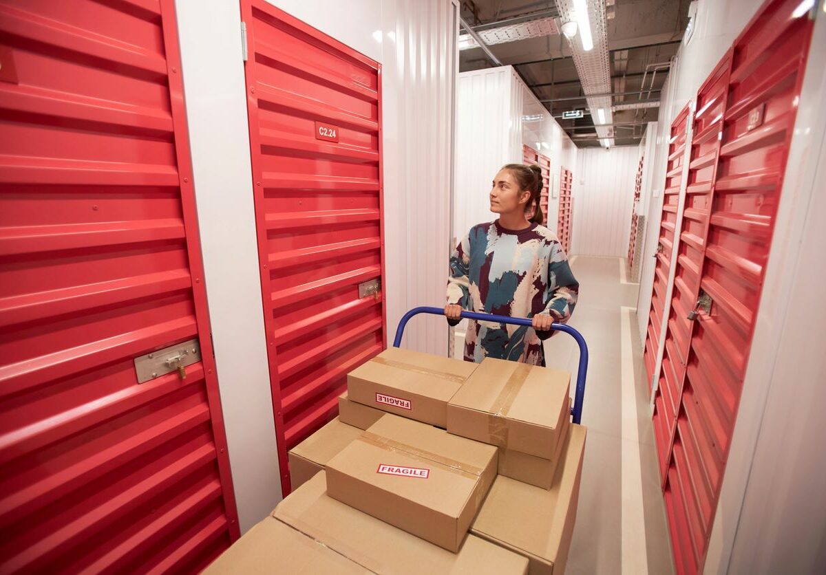 A young woman pushing a handcart with boxes in a storage facility.