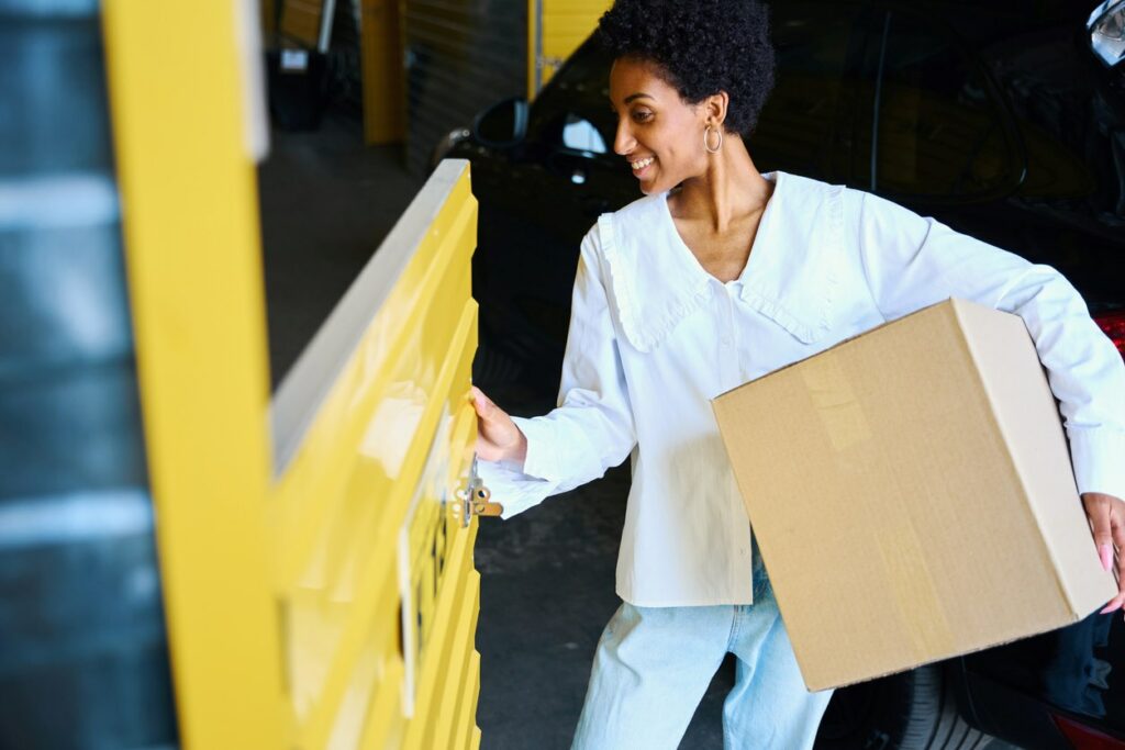 A smiling young woman loads a box into a storage locker.