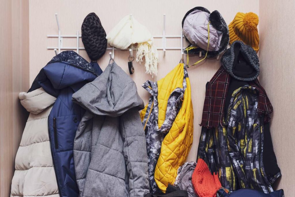 Many winter coats, caps, and hats are hanging in a mess on hooks in a corridor.