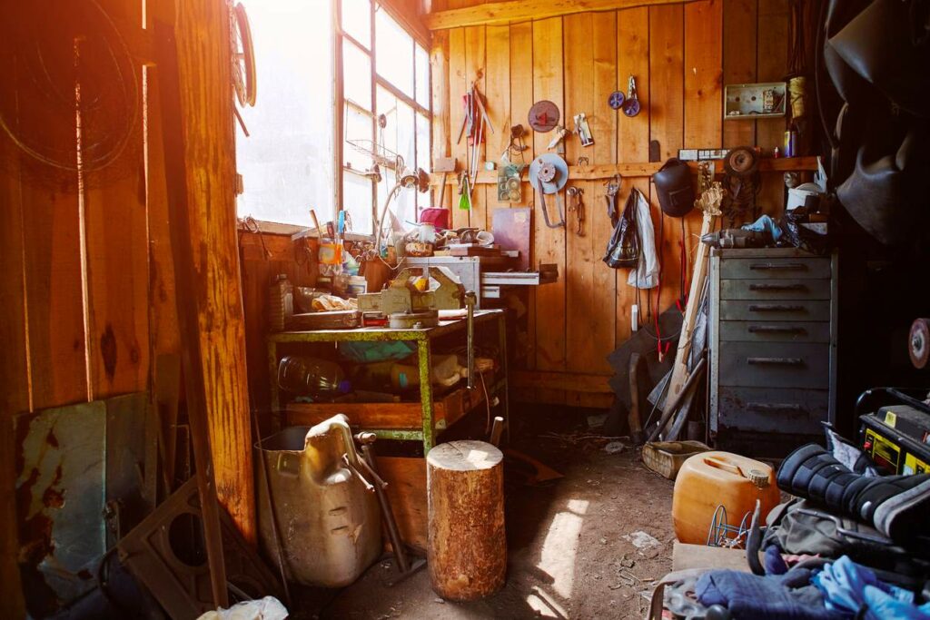 A wooden garage cluttered with tools on the floor and walls.