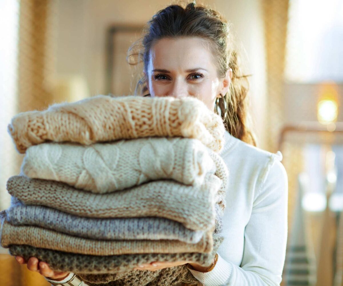 A woman with a stack of seasonal sweaters, preparing them for storage.