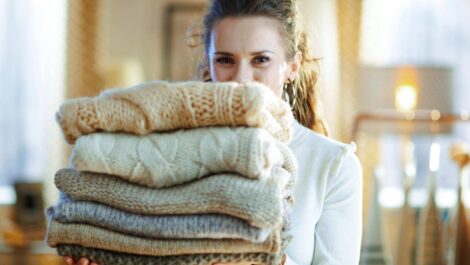 A woman with a stack of seasonal sweaters, preparing them for storage.