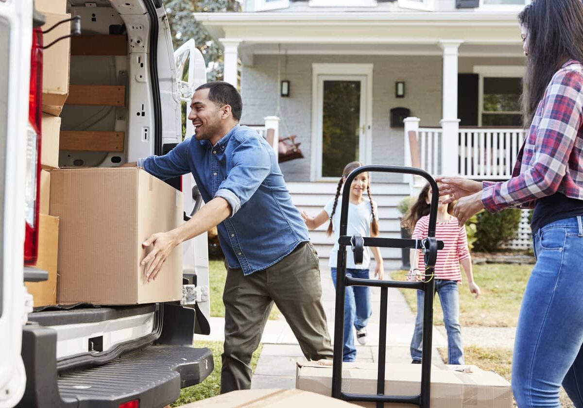 A family unpacking a moving truck in front of their new home.
