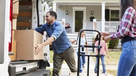 A family unpacking a moving truck in front of their new home.