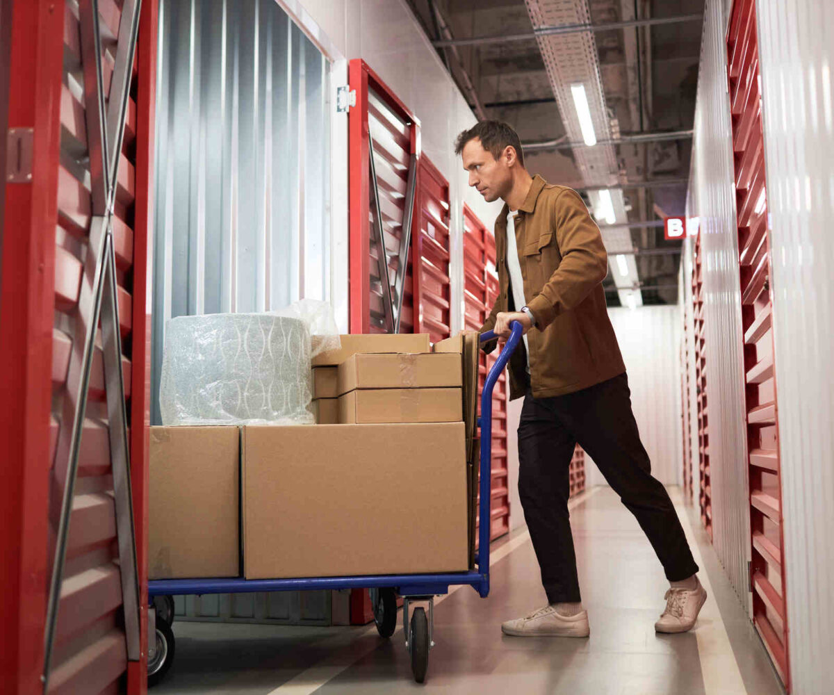 A person bringing boxes and wrapped storage items into their storage unit.