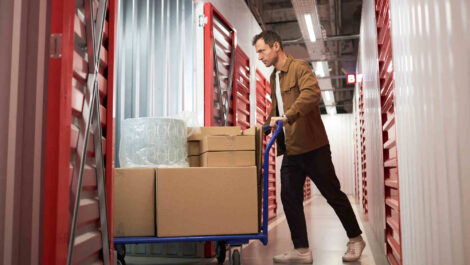 A person bringing boxes and wrapped storage items into their storage unit.