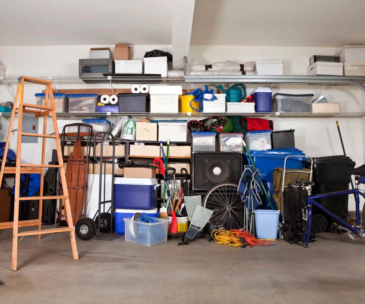 A garage prior to being remodeled, with a variety of items stowed within, including a ladder, a bike, and a couple of coolers.