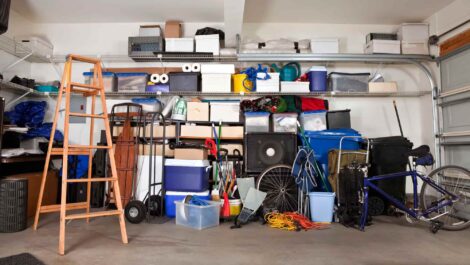 A garage prior to being remodeled, with a variety of items stowed within, including a ladder, a bike, and a couple of coolers.